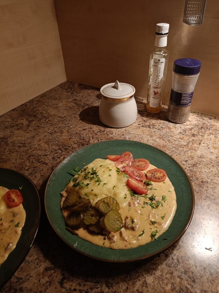 Creamy beef stroganoff with mashed potatoes, pickles, and cherry tomatoes served on a green plate.