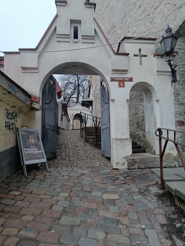 Lühike Jalg passage in Tallinn Old Town, with a medieval archway, cobbled pathway, and stone walls leading uphill.