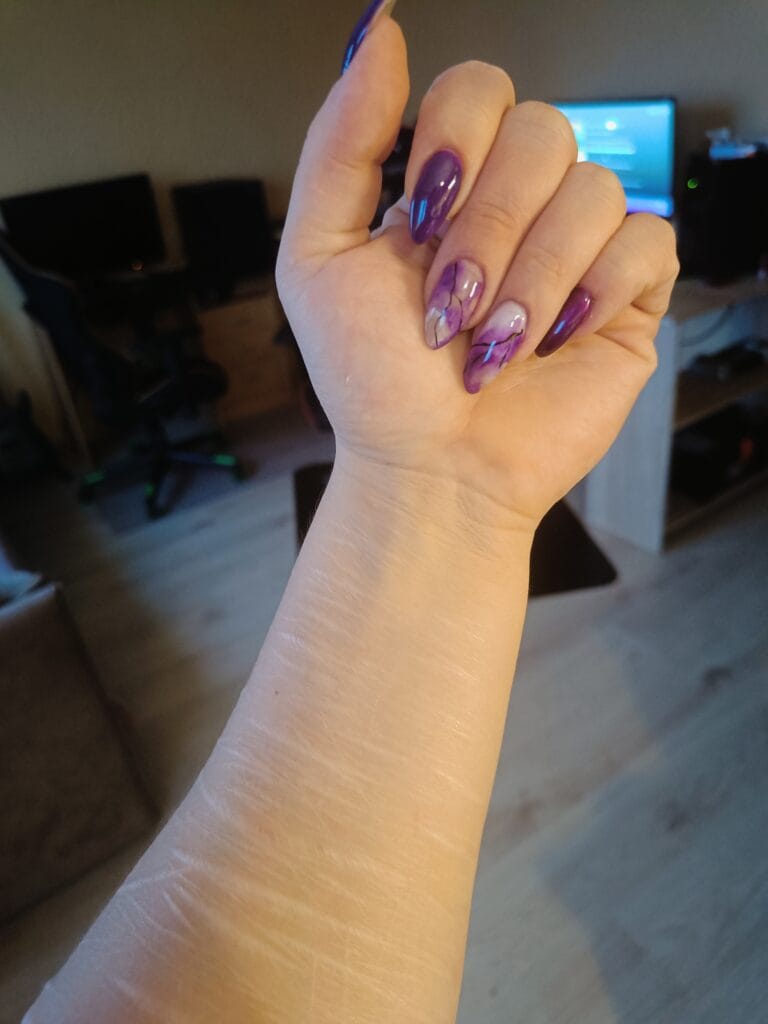 Purple marble-effect gel manicure on almond-shaped nails, photographed indoors with a home office softly blurred in the background.