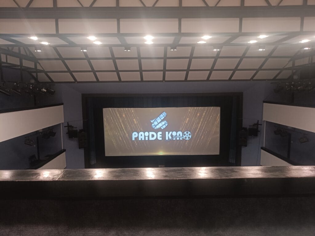 The view from the upper balcony of Paide Cinema before a movie screening. The large screen displays the Paide Kino logo, while the theatre stretches out below beneath bright ceiling lights.