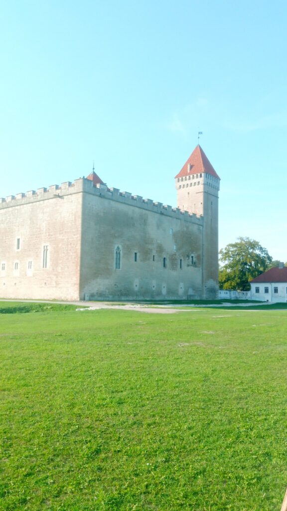 Kuressaare Castle on a bright summer day, with its pale stone walls, red-roofed towers, and a wide green lawn stretching across the foreground.