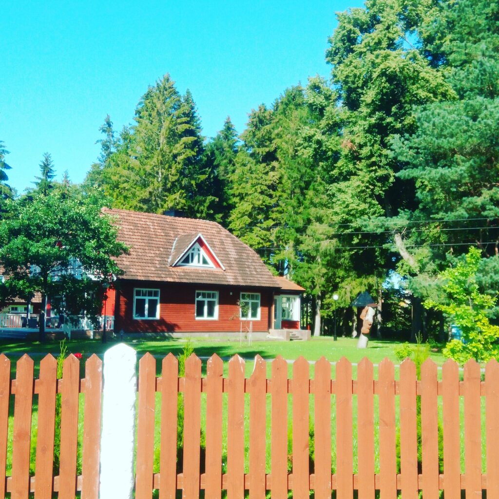 Traditional red wooden house surrounded by tall trees and a neatly kept garden on the island of Hiiumaa.